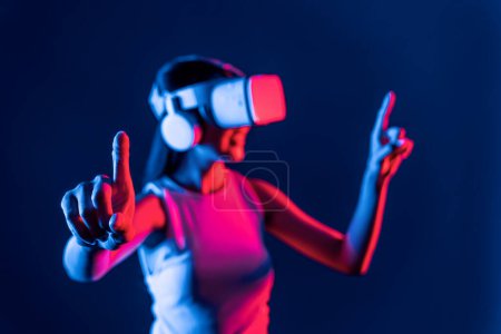 Téléchargez les photos : Support féminin intelligent avec entouré de néon cyberpunk lumière usure VR casque connectant métaverse, technologie futuriste communauté cyberespace. Femme utilisant un objet virtuel pointant du doigt. Hallucination. - en image libre de droit