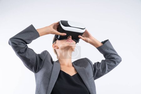 Téléchargez les photos : Femme d'affaires compétente regardant le monde de la réalité visuelle en utilisant le verre VR tout en se tenant à l'arrière-plan. Smart manager détenant un masque VR pour connecter metaverse en utilisant l'innovation technologique. Machines et appareils. - en image libre de droit