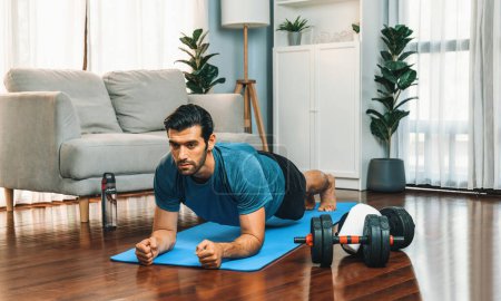 Photo for Athletic and sporty man doing plank on fitness mat during home body workout exercise session for fit physique and healthy sport lifestyle at home. Gaiety home exercise workout training. - Royalty Free Image