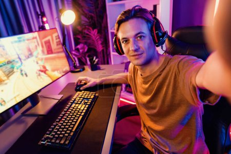 Host-Kanal von Smart-Gaming-Streamer, der in die Kamera schaut, mit spielender Kampfmannschaft, die im Hintergrund auf Kriegsschiff schießt, auf dem Bildschirm auf der Rückseite, mit Headset im digitalen Neon-Cyber-Raum. Pekuniär.