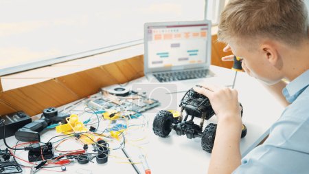 Photo for Top view of happy student study car model construction at table with electronic equipment and laptop display coding program screen scatter around at STEM classroom. Creative education. Edification. - Royalty Free Image