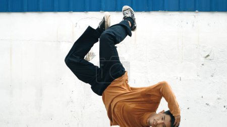 Foto de El hombre hispano estira los brazos y baila break bailando frente a la pared. Motion shot de bailarina callejera con estilo en traje casual que practica el baile en estilo hip hop. Deporte al aire libre 2023. Antecedentes Endeavor. - Imagen libre de derechos
