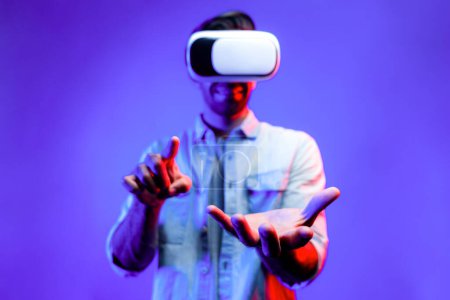 Foto de Hombre elegante caucásico con gafas VR mientras sostiene la exhibición del holograma en VR. Persona feliz sosteniendo y señalando mientras mira usando gafas y auriculares con fondo de luz de neón. Tecnología. Desviación. - Imagen libre de derechos