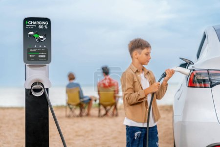 Photo for Family vacation trip traveling by the beach with electric car, little boy recharge EV car while his family enjoy seascape beach. Family trip with alternative energy and eco-friendly car. Perpetual - Royalty Free Image
