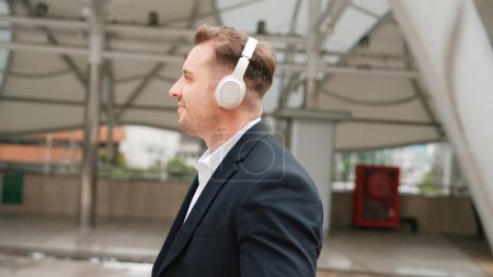 Happy business man using headphone listening relax music and move along music while walking at street in urban city with lively mood. Manager wear headset and enjoying listen relaxing rhyme. Urbane.