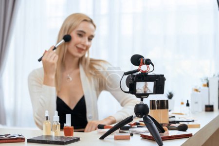 Photo for Young woman making beauty and cosmetic tutorial video content for social media. Beauty blogger smiles to camera while showing how to apply mascara to audience or followers. Blithe - Royalty Free Image