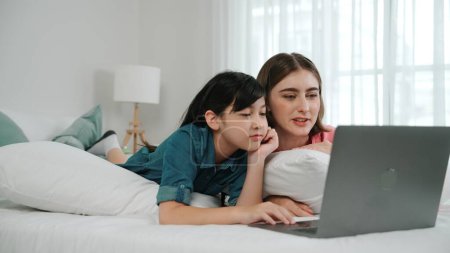 Photo for Attractive daughter and caucasian mother watching movie at laptop screen while lie on bad. Happy family spend time together before bed time. Parent and cute girl enjoy playing games together Pedagogy. - Royalty Free Image