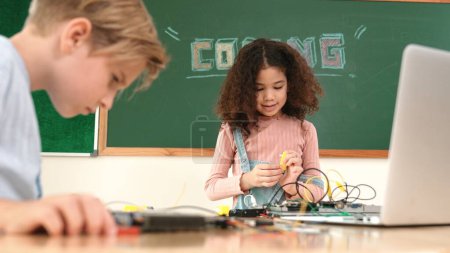 Photo for Girl standing while fixing electronic board by using screwdriver. American student and happy caucasian boy working together to inspect electric system. Curious children working on board. Pedagogy. - Royalty Free Image