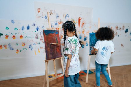Téléchargez les photos : Les élèves peignant sur toile montrent des compétences d'artiste en classe de dessin. Les enfants peignent des toiles autour des pinceaux dont la couleur principale est le bleu et le rouge. Papier peint imprimé à la main d'enfants. Erudition. - en image libre de droit