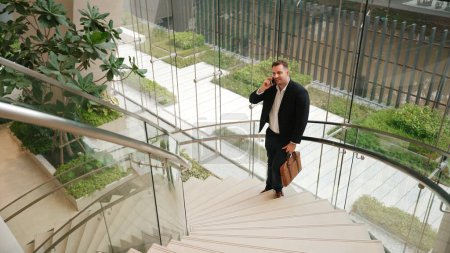Téléchargez les photos : Homme d'affaires caucasien appelant gestionnaire en utilisant un téléphone intelligent et discuter de rapport financier. Leader masculin parlant équipe de marketing en utilisant le téléphone tout en se tenant à l'escalier dans le bâtiment moderne. Urbane. - en image libre de droit