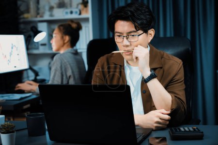 Photo for Businessman with stressful face working on laptop waiting email while coworker trading stock exchange investment at late night time at modern office, working on startup company project job. Infobahn. - Royalty Free Image