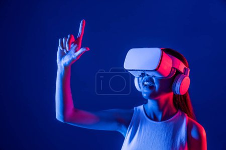 Téléchargez les photos : Femme debout entouré de néon lumière usure VR casque connectant métaverse, technologie futuriste de la communauté du cyberespace, indice de propagation et pouce doigt interagissant objet virtuel. Hallucination. - en image libre de droit