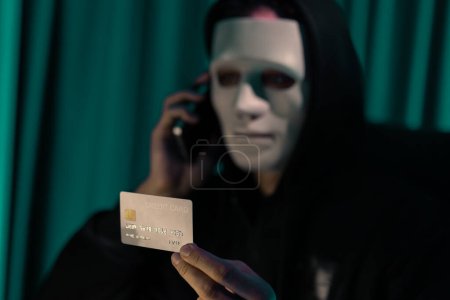 Foto de Máscara blanca criminal anónimo llamando al dueño de la tarjeta de crédito para amenazar rescate con la información de privacidad de toda la base de datos, haciendo cifrado de contraseña mediante la programación hackear tratando de hacer inseguro. Pecuniario. - Imagen libre de derechos