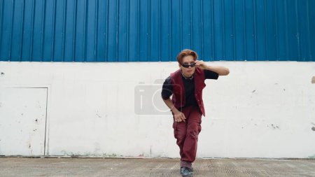 Foto de Guapo bailarín callejero practicando break dance en el fondo blanco. Hombre de deporte con estilo hip hop mientras mueve los pasos a la música en la calle con fondo azul. Deporte al aire libre 2024. Endeavor. - Imagen libre de derechos