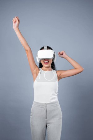 Téléchargez les photos : Femme intelligente debout avec fond gris portant casque VR connectant métaverse, technologie futuriste de la communauté du cyberespace. Femme élégante excitée de voir généré des paysages virtuels. Hallucination. - en image libre de droit