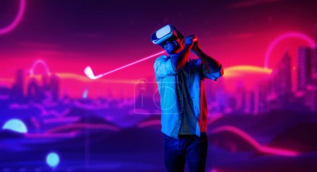 Téléchargez les photos : Homme caucasien jouant au golf en métaverse tout en portant des lunettes VR pour entrer dans le monde virtuel simulé. Beau joueur utilisant des lunettes de réalité virtuelle entrer dans le terrain de golf néon. L'innovation. Du sport. Déviation. - en image libre de droit