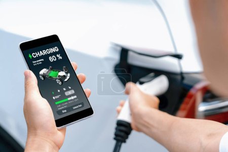 Hand einlegen EV-Ladegerät Stecker in Elektrofahrzeug zum Aufladen EV Auto, Batterie-Statusanzeige auf Smartphone EV-Anwendung. Künftige alternative saubere und nachhaltige Energie für den Transport. Unvergänglich