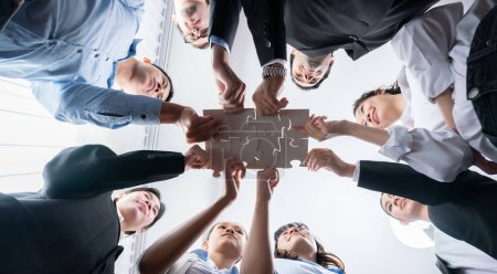 Téléchargez les photos : Des hommes d'affaires multiethniques tenant des pièces de puzzle et les fusionnant en tant que solution efficace pour résoudre le travail d'équipe, la vision partagée et l'objectif commun combinant divers talents. En dessous. Habillement - en image libre de droit