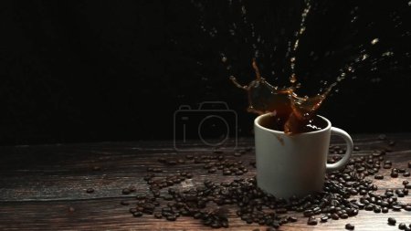Téléchargez les photos : Mouvement super lent de chute de glace tombant dans la tasse de café et éclaboussures avec fond noir séparé. Gros plan de la goutte de sucre dans l'espresso entouré d'une pile de grains de café. Coup de feu. Comestible. - en image libre de droit