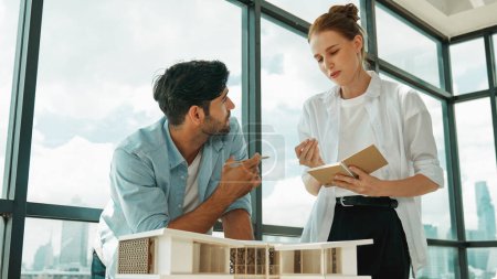 Photo for Skilled architect engineer team discussion about house model construction. Smart interior designer sharing, talking about building design while beautiful coworker taking a note. Design. Tracery - Royalty Free Image