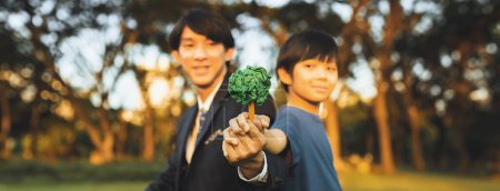 Téléchargez les photos : Garçon asiatique et homme d'affaires tenant l'arbre de papier ensemble comme concept du Jour de la Terre en tant qu'entreprise sociale responsable de rendre la protection de l'environnement plus verte pour la génération future durable. Panorama. Pneumatique - en image libre de droit
