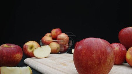 Foto de Macrografía de manzanas exhibidas en varias formas: enteras, cortadas en rodajas, y dentro de un recipiente de vidrio con fondo negro. Cada primer plano captura los colores rojos de las manzanas en la tabla de cortar. Comestible. - Imagen libre de derechos