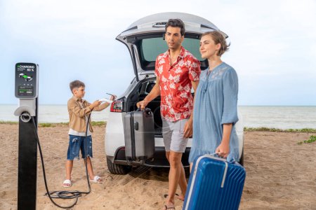 Photo for Family vacation trip traveling by the beach with electric car, lovely family taking luggage out while charging EV car battery with clean energy. Alternative family travel by eco-friendly car.Perpetual - Royalty Free Image