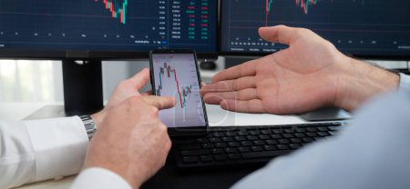 Photo for Cropped photo of exchange traders pointing lowest chart stage on dynamic graph with smartphone on panorama view, analyzing comparing with monitor and phone, discussing financial technology. Sellable. - Royalty Free Image