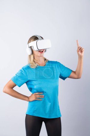 Photo for Girl pointing or spinning basketball while using VR glasses. Caucasian woman flexing while wearing casual shirt and visual reality goggles and standing at pink background. Innovation. Contraption. - Royalty Free Image