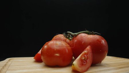 Téléchargez les photos : Macrographie, tranches de tomate reposent élégamment sur une planche à découper rustique sur un fond noir dramatique. Chaque gros plan capture la texture juteuse et les couleurs riches des tomates. Comestible. - en image libre de droit