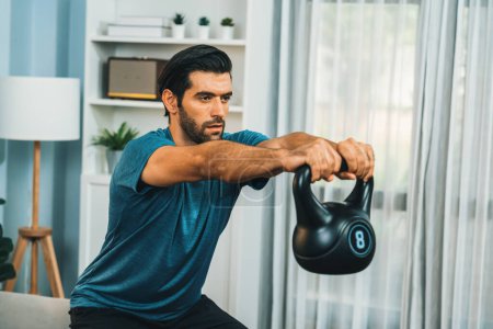 Photo for Athletic body and active sporty man doing squat with kettlebell weight for effective targeting muscle gain at gaiety home as concept of healthy fit body home workout lifestyle. - Royalty Free Image