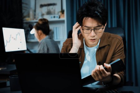 Photo for Businessman with stressful face looking on document file deadline while coworker trading stock exchange investment at late night time at modern office working on startup company project job. Infobahn. - Royalty Free Image