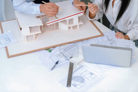 Ingeniero profesional mide el modelo de la casa, mientras que el diseñador experto escribe en el plano. Trabajen juntos, colaboren, cooperen. Diseño creativo y concepto de trabajo en equipo. Vista superior. Inmaculada.
