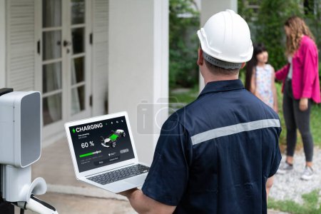 Photo for Qualified technician working on home EV charging station installation, making troubleshooting and configuration setup on charging system with laptop for EV at home with the family present. Synchronos - Royalty Free Image
