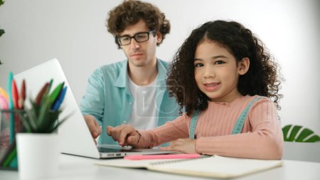 Photo for American student looking at camera while working on laptop with dad sitting and looking at laptop screen to check engineering code. Happy school girl smiling while study about generate ai. Pedagogy. - Royalty Free Image