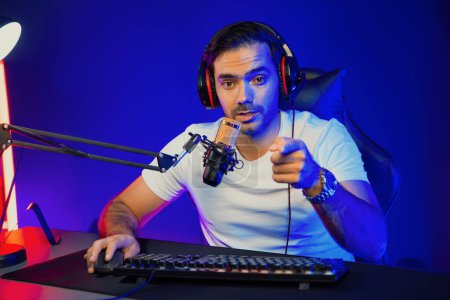 Smart gaming streamer looking at camera with trendy pose, passing the level of online game user on pc, using headset and mic for communicate with others at digital neon light studio room. Surmise.