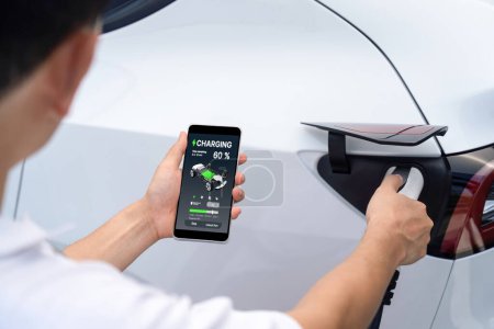 Branchez le chargeur EV main dans le véhicule électrique pour recharger la voiture EV, affichage de l'état de la batterie sur l'application smartphone EV. Énergie propre et durable future pour les transports. Perpétuel