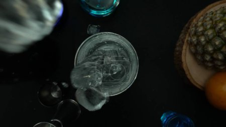 Blick von oben auf qualifizierte Barkeeper Hand bereiten martini mit Oliven garniert. Nahaufnahme von Hand machen transparenten Cocktail-Drink mit Oliven mit Bewegung und schwarzem Hintergrund. Makrographie. Komestibel.