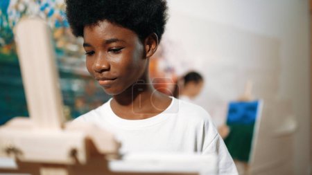 Photo for Closeup of african boy hand paint canvas with warm tone color while caucasian girl in casual outfit drawing cool tone colors behind at colorful stained wall. Creative activity concept. Edification. - Royalty Free Image