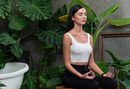 Mujer joven haciendo yoga matutino y meditación en jardín natural con hoja de planta, disfrutando de la soledad y practicando poses meditativas. Actividad de atención plena y estilo de vida mental saludable. Blithe.