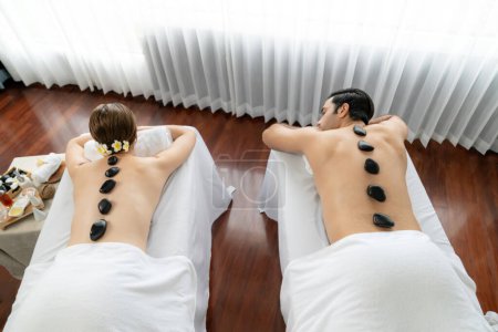 Photo for Hot stone massage at spa salon in luxury resort with day light serenity ambient, blissful couple customer enjoying spa basalt stone massage glide over body with soothing warmth. Quiescent - Royalty Free Image