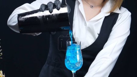 Macrography, experience the artistry of a skilled bartenders hand as they expertly pouring a Blue Hawaii cocktail in glass against a striking black background. Cocktail. Close-up shot. Comestible.