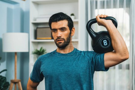 Photo for Athletic body and active sporty man lifting kettlebell weight for effective targeting muscle gain at gaiety home as concept of healthy fit body home workout lifestyle. - Royalty Free Image