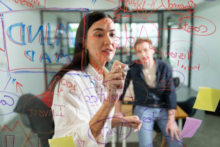Photo for Professional business team brainstorming and working together about marketing project. Female caucasian leader writing idea on stick note while coworker present her idea confidently. Immaculate. - Royalty Free Image