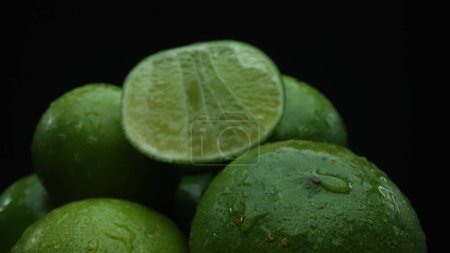 Slices of lime are meticulously arranged in a pile, set against a black background. Each lime slice is captured in stunning detail, its vibrant green hue and enticing texture. Close up. Comestible.