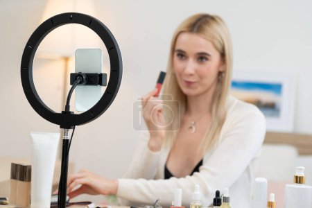 Photo for Young woman making beauty and cosmetic tutorial video content for social media. Beauty blogger using camera and light ring while showing how to apply liquid lipstick to audience or follower. Blithe - Royalty Free Image