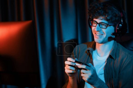 Photo for Smiling young gaming streamer team playing with joystick on Esport online on pc fighting game, try to win competitors on strategy planning for next harder at red neon lighting modern room. Gusher. - Royalty Free Image