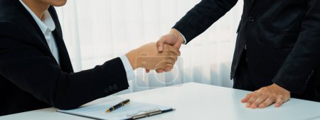 Two business executive shake hand in boardroom, sealing agreement merging two company. Handshake symbolize business partnership and cooperation. Corporate acquisition and merger concept. Shrewd
