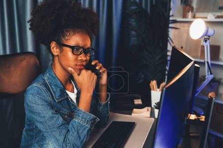 Photo for Amazed young African woman looking on screen monitor laptop, calling with friend on smartphone, wearing jeans shirt. Thinking the job project planing or study new technology at workplace. Tastemaker. - Royalty Free Image