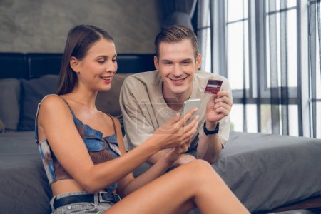 Photo for Young couple sit in the home bedroom using online payment app and digital wallet on smartphone to pay with credit card. E commerce shopping and modern purchasing via mobile internet. Unveiling - Royalty Free Image
